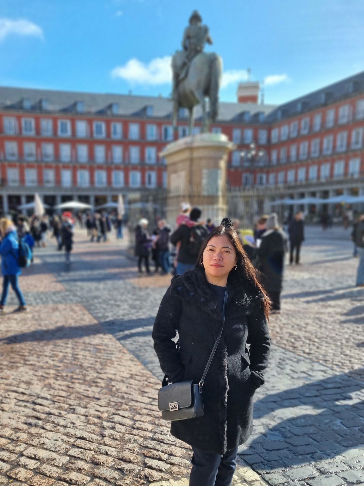 Anselma Benítez sonriendo en la Plaza Mayor de Madrid, con la estatua ecuestre y las fachadas rojizas al fondo
